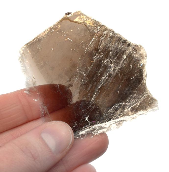 Mão segurando um pedaço irregular de mica, do tamanho de um biscoito cream cracker, o mineral é tão fino que é transparente em algumas partes.